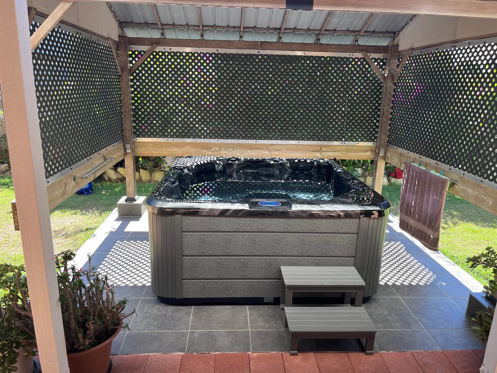Spa under a timber pergola with a lattice screen, beside a back lawn